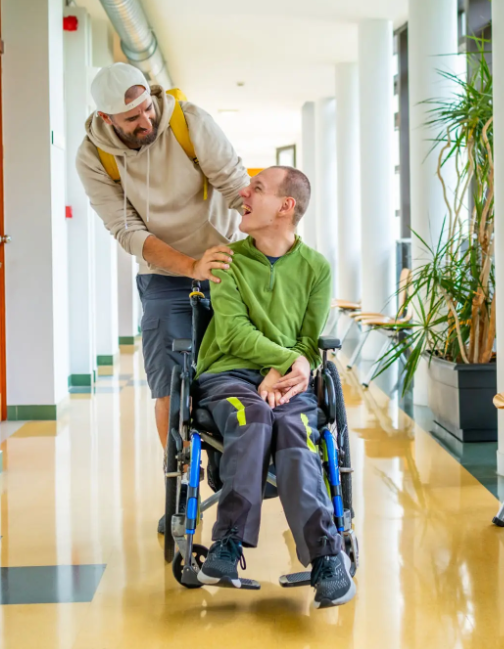 A support worker walking alongside a person in a wheelchair in a bright, modern hallway